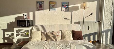 A bedroom with a bed, a bedside table with a microwave, and a lamp. There are three framed pictures on the wall.