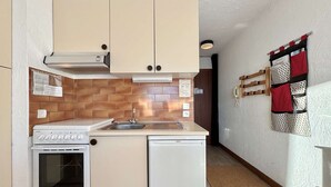 A compact kitchen with a stove, oven, and dishwasher, a wooden backsplash, and a red and white quilt hanging on the wall.