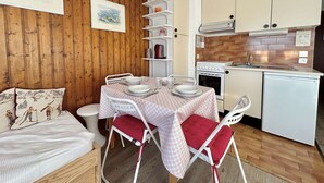 A compact kitchen with a dining area, wooden walls, and a small dining table set for four.