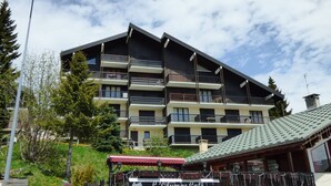 A multi-story building with balconies, a sign for 'L'Olympe Café' indicating a restaurant, and a small adjacent building with a green roof. - 2-Room Apt - 5 people, Les Saisies, Pets allowed (Les Saisies)