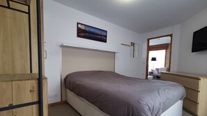 A bedroom with a bed, wooden wardrobe, desk, and a TV mounted on the wall. - Renovated apartment for 4, near center, parking (Les Gets)