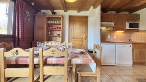 Ein Holztisch mit Stühlen, eine Küchenzeile mit Mikrowelle und Geschirrspüler sowie ein Fenster mit Vorhängen.