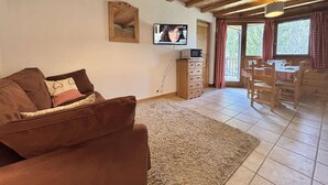 Ein gemütliches Wohnzimmer mit einem braunen Sofa, einem Flachbildfernseher und einer Holzbalkendecke.