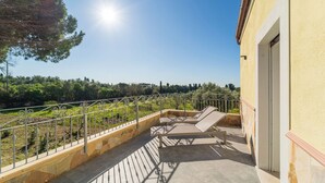 Ein Balkon mit einer Steinmauer, einem Metallgeländer und Blick auf einen Weinberg.