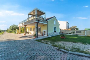 A two-story house with a balcony, a paved driveway, and a well-maintained lawn.