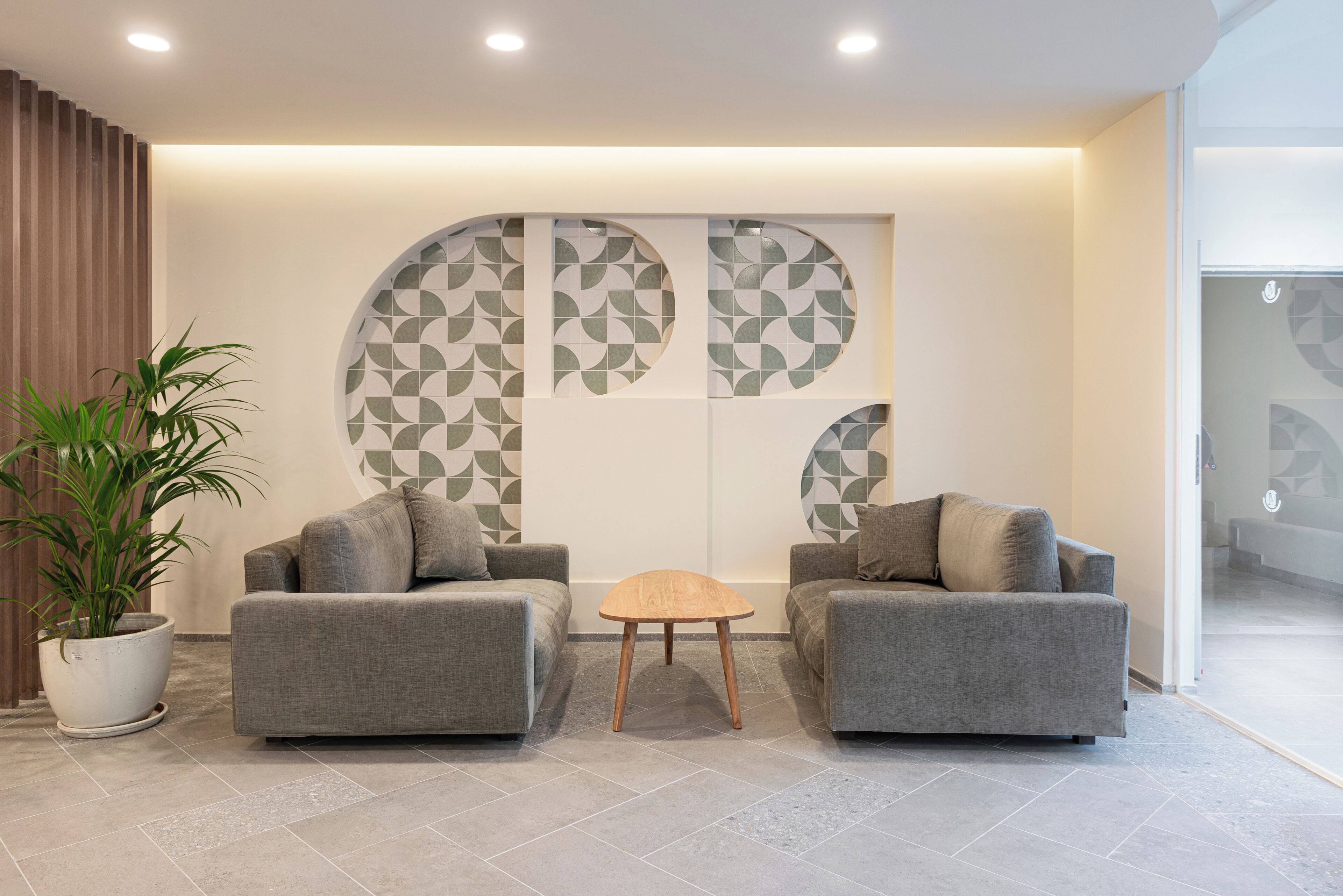 Un hall moderno con dos sofás grises, una mesita de madera y una gran pared decorativa con patrones geométricos.