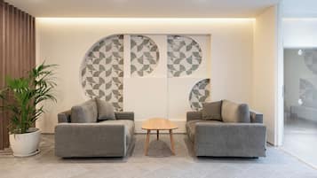 Un hall moderno con dos sofás grises, una mesita de madera y una gran pared decorativa con patrones geométricos.