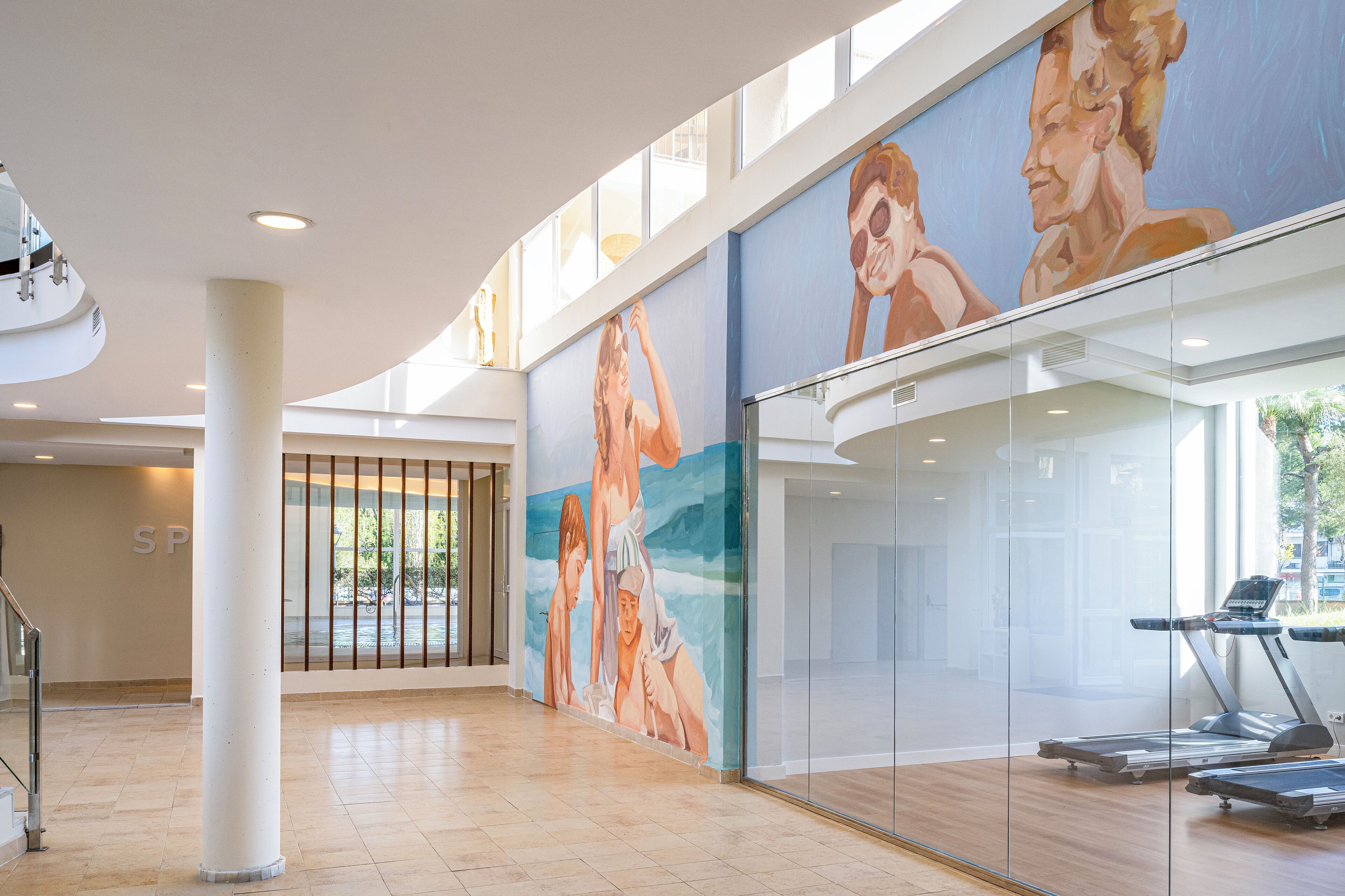 Un vestíbulo espacioso con un mural grande, una pared de vidrio y una cinta de correr.