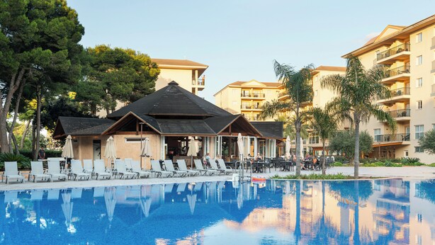 A swimming pool with lounge chairs and umbrellas, surrounded by multi-story buildings with balconies. - Aparthotel Can Picafort Palace (Santa Margalida)