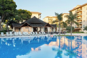A swimming pool with lounge chairs and umbrellas, surrounded by multi-story buildings with balconies. - Aparthotel Can Picafort Palace (Santa Margalida)