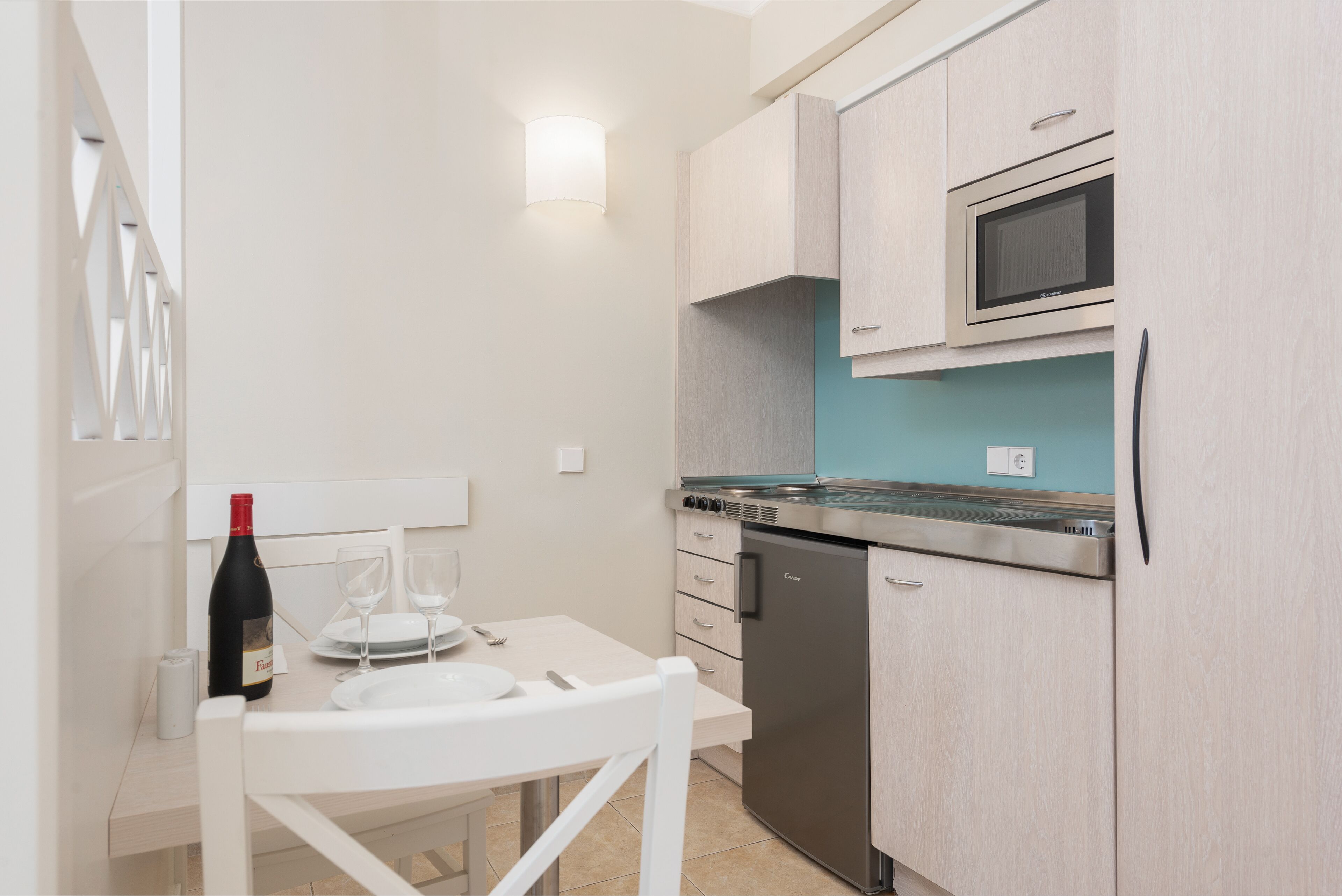 A compact kitchen with a microwave, dishwasher, and a small dining table set with plates and a wine bottle.