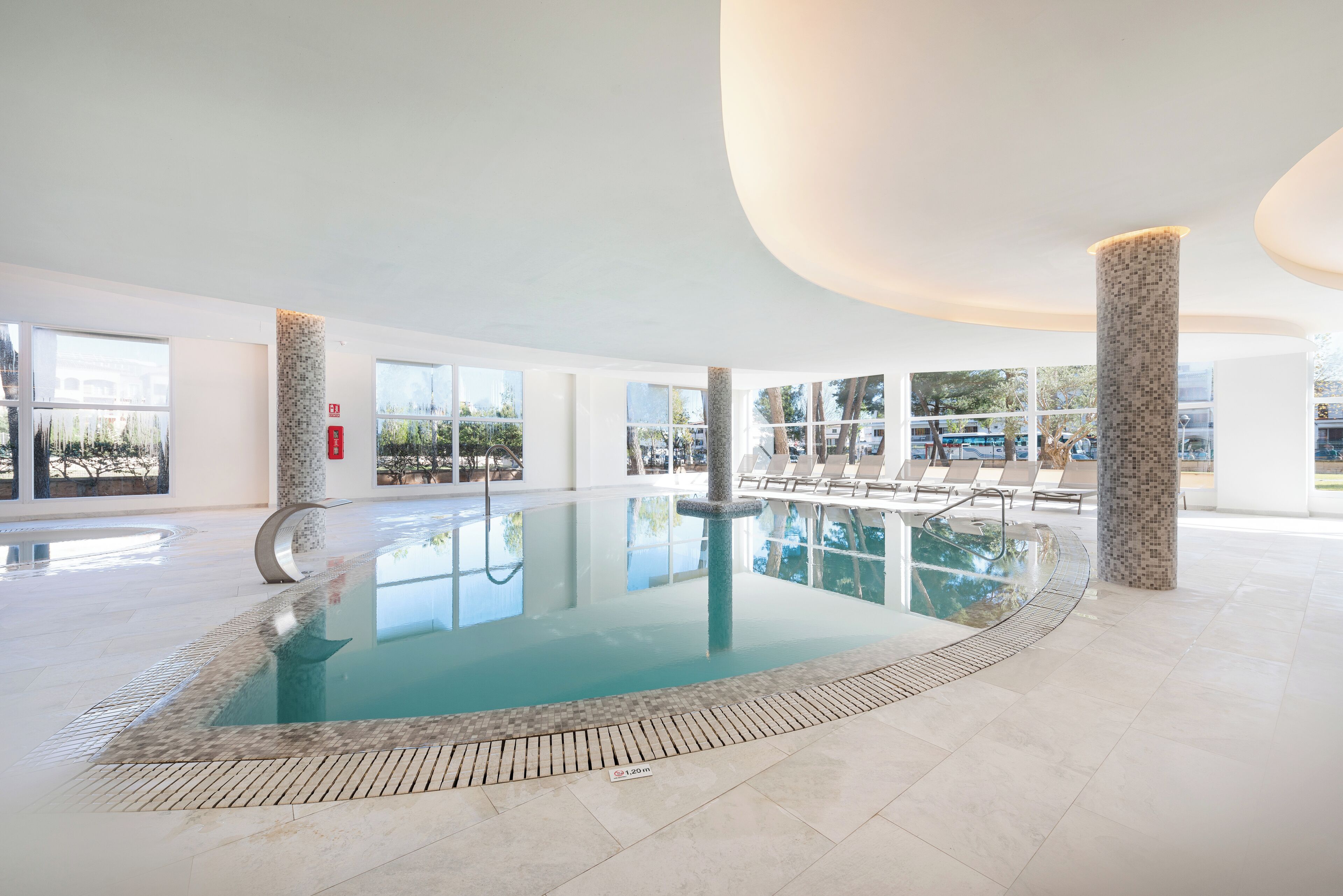 A modern indoor swimming pool with clear water, surrounded by white walls and large windows.