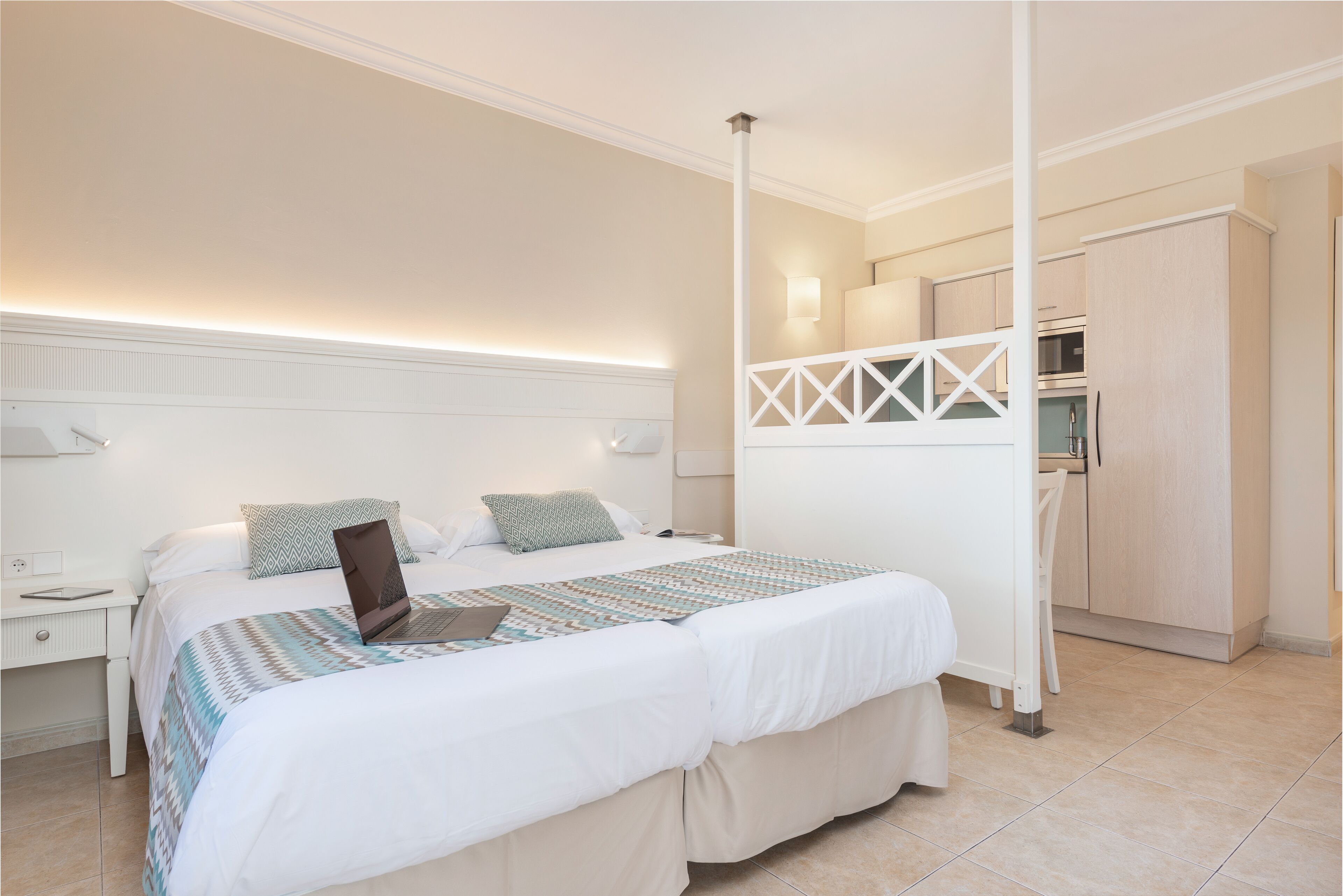 Ein modernes Hotelzimmer mit einem großen Bett, einem Schreibtisch mit Laptop, einer Küchenzeile und einem Badezimmer.
