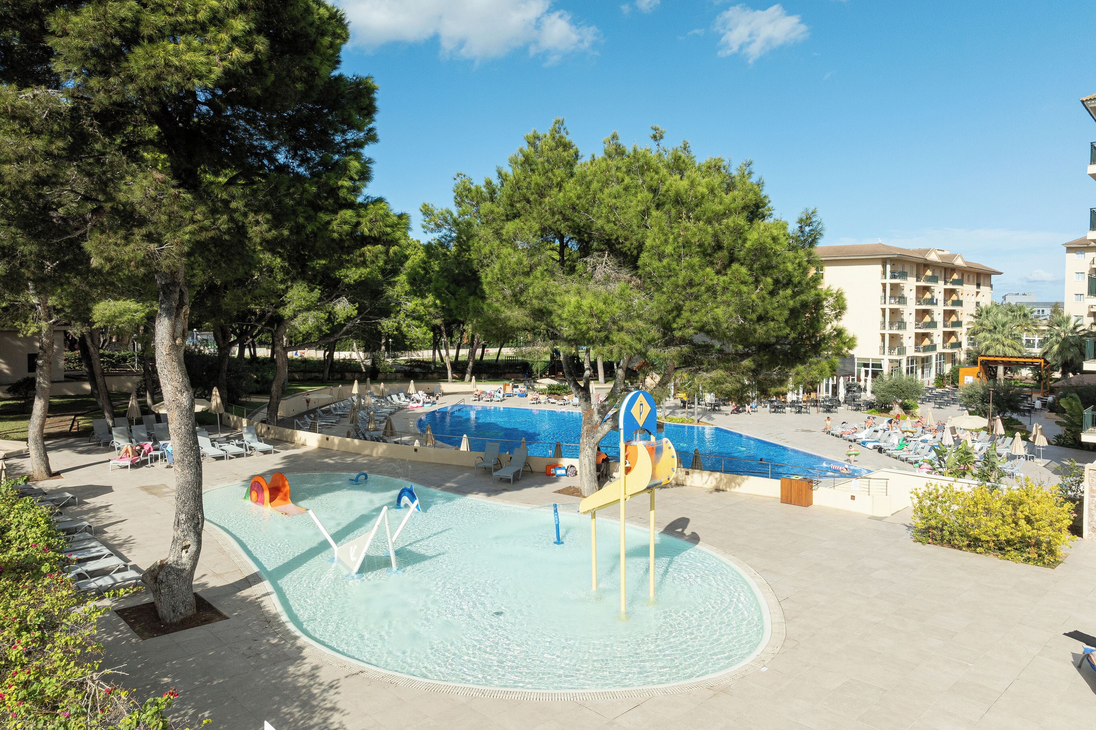 A pool area with a water slide, lounge chairs, and a building in the background.