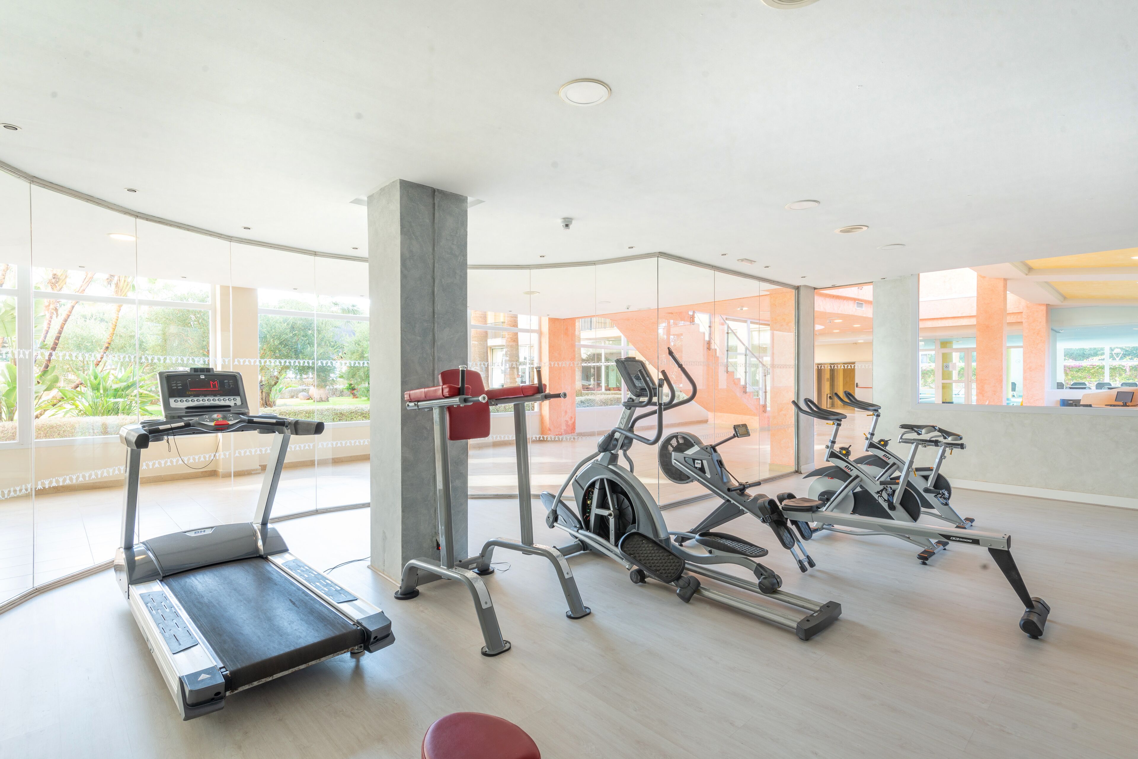 A modern gym with treadmills, elliptical machines, and a red bench.