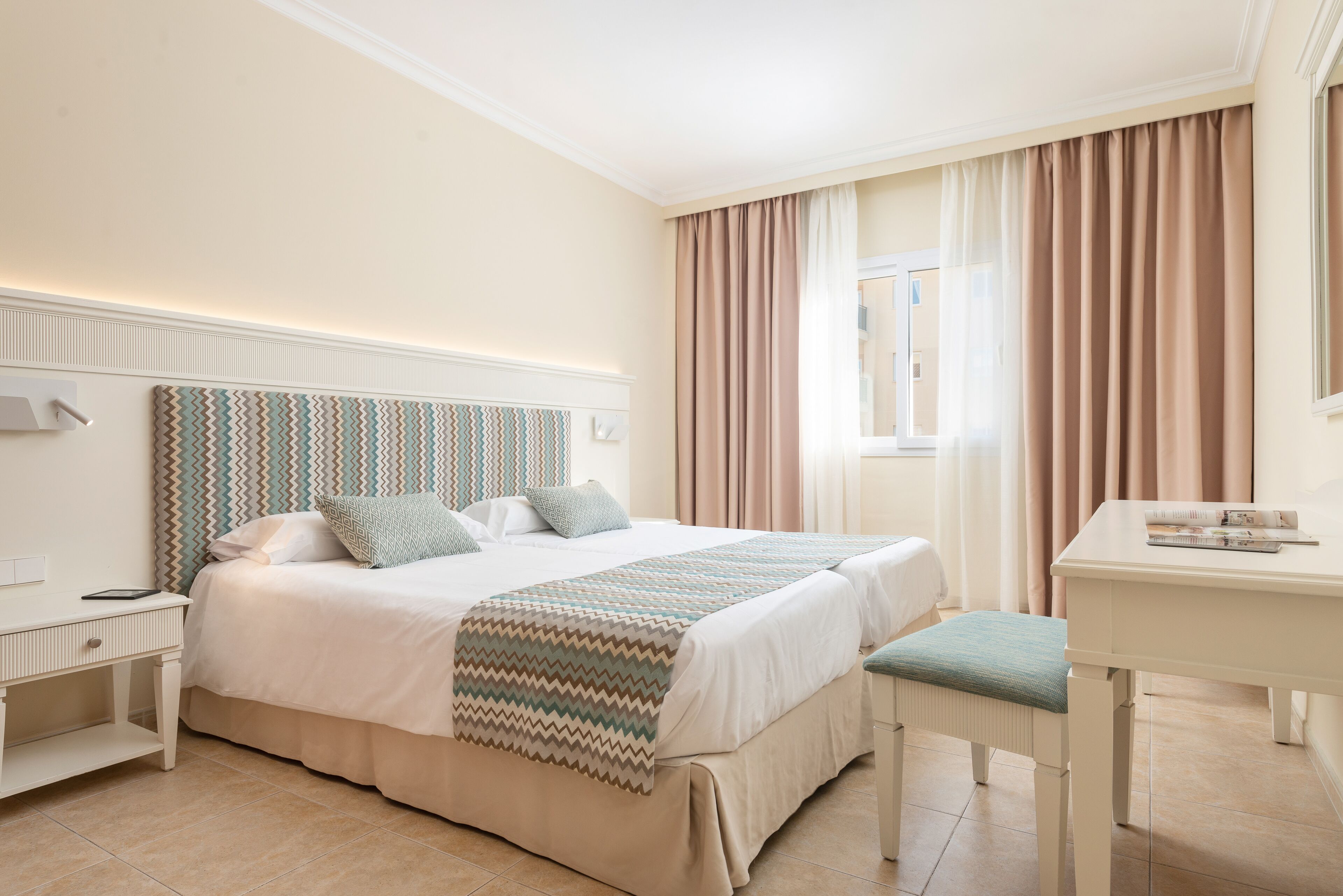 Ein Hotelzimmer mit Bett, Nachttisch, Sessel und Schreibtisch.