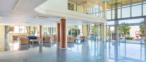 A spacious lobby with a high ceiling, large windows, and a central seating area with sofas and chairs.