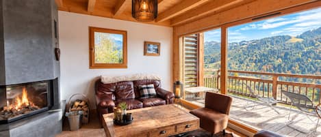 A cozy living room with a fireplace, leather sofa, wooden coffee table, and a scenic mountain view through large windows.