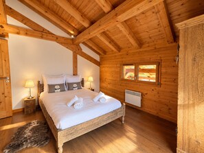A wooden cabin bedroom with a bed, two bedside lamps, a fur rug, and a window with a view.