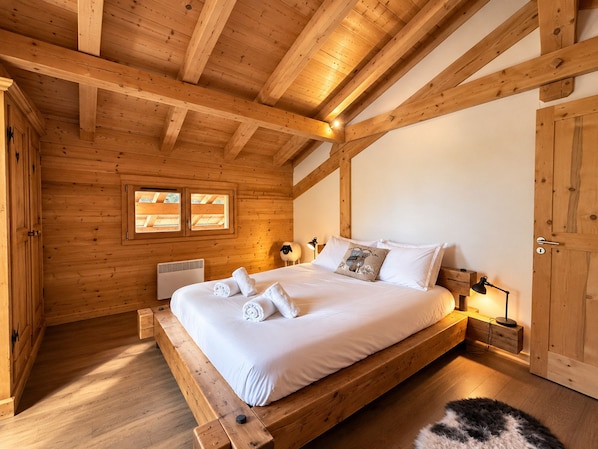 A wooden cabin bedroom with a bed, a window, a heater, and a door.
