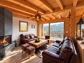 A cozy cabin interior with a fireplace, leather furniture, and a scenic mountain view.
