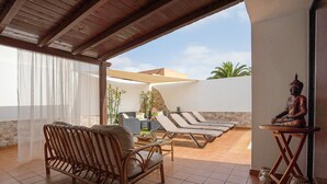 Eine überdachte Terrasse mit Korbmöbeln, einer Buddha-Statue und Blick auf den Garten.