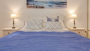 Ein Bett mit blauer Decke, zwei Nachttischlampen und ein Gemälde eines Leuchtturms an der Wand.