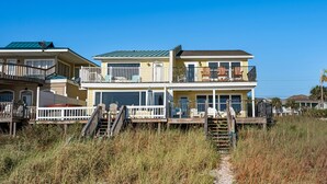 A multi-story beachfront house with balconies, a deck, and a pathway leading to the entrance.
