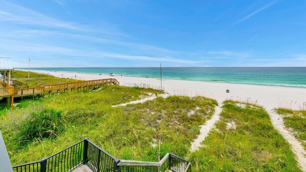A beach with a wooden boardwalk and grassy areas leading to the shore.