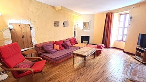 A living room with a wooden floor, a red armchair, a purple sofa, a wooden coffee table, and a television on a stand. - Duplex with terrace & patio – old town Saint-Paul-Trois-Châteaux (Saint-Paul-Trois-Châteaux)