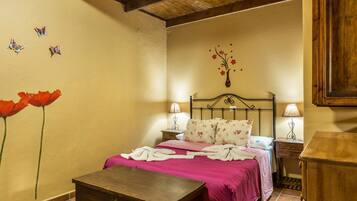 Un dormitorio con una cama, mesitas de noche, un banco de madera y una pared decorada con motivos florales.