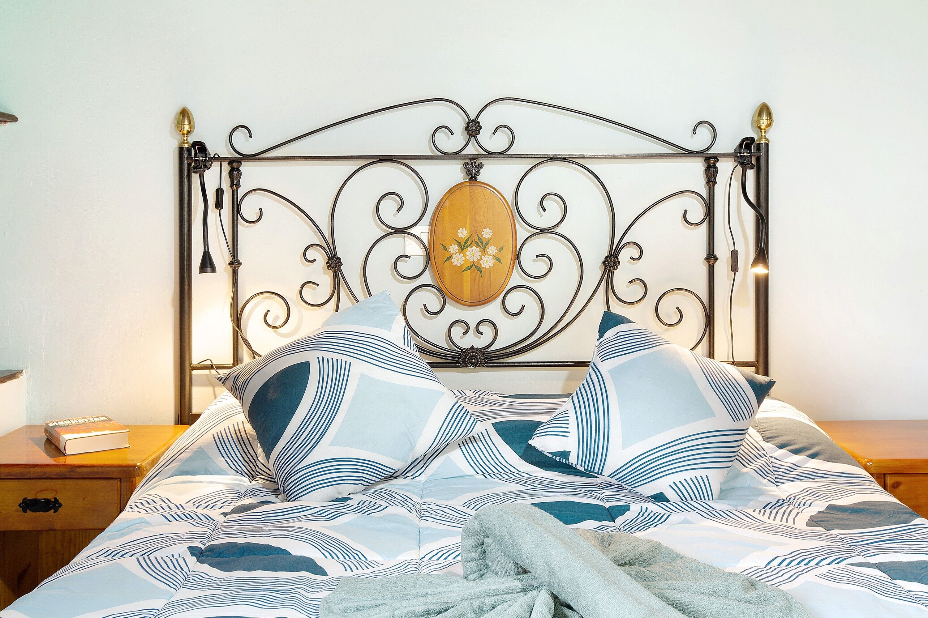 Una cama con cabecera de metal, una placa de madera y ropa de cama a rayas.