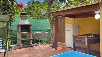 Eine Terrasse im Freien mit einem Grill, einem Tischkicker und einem Pingpongtisch.