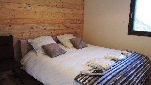 Une chambre d’hôtel avec une tête de lit en bois, un lit avec du linge de lit blanc, deux oreillers, une couverture à rayures et une chaise.
