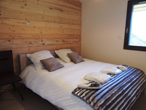 Habitación de hotel con cabecera de madera, cama con ropa blanca, dos almohadas, manta a rayas y una silla.