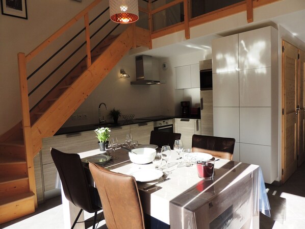 A dining area with a wooden staircase, a kitchen in the background, and a table set for four. - T3 in Les Gets, view of the slopes (Les Gets)