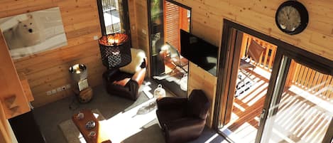 Un intérieur de chalet chaleureux avec des murs en bois, une cheminée, un téléviseur et une grande fenêtre.