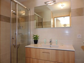 A modern bathroom with a glass shower enclosure, a wooden vanity, a large mirror, and a potted plant.