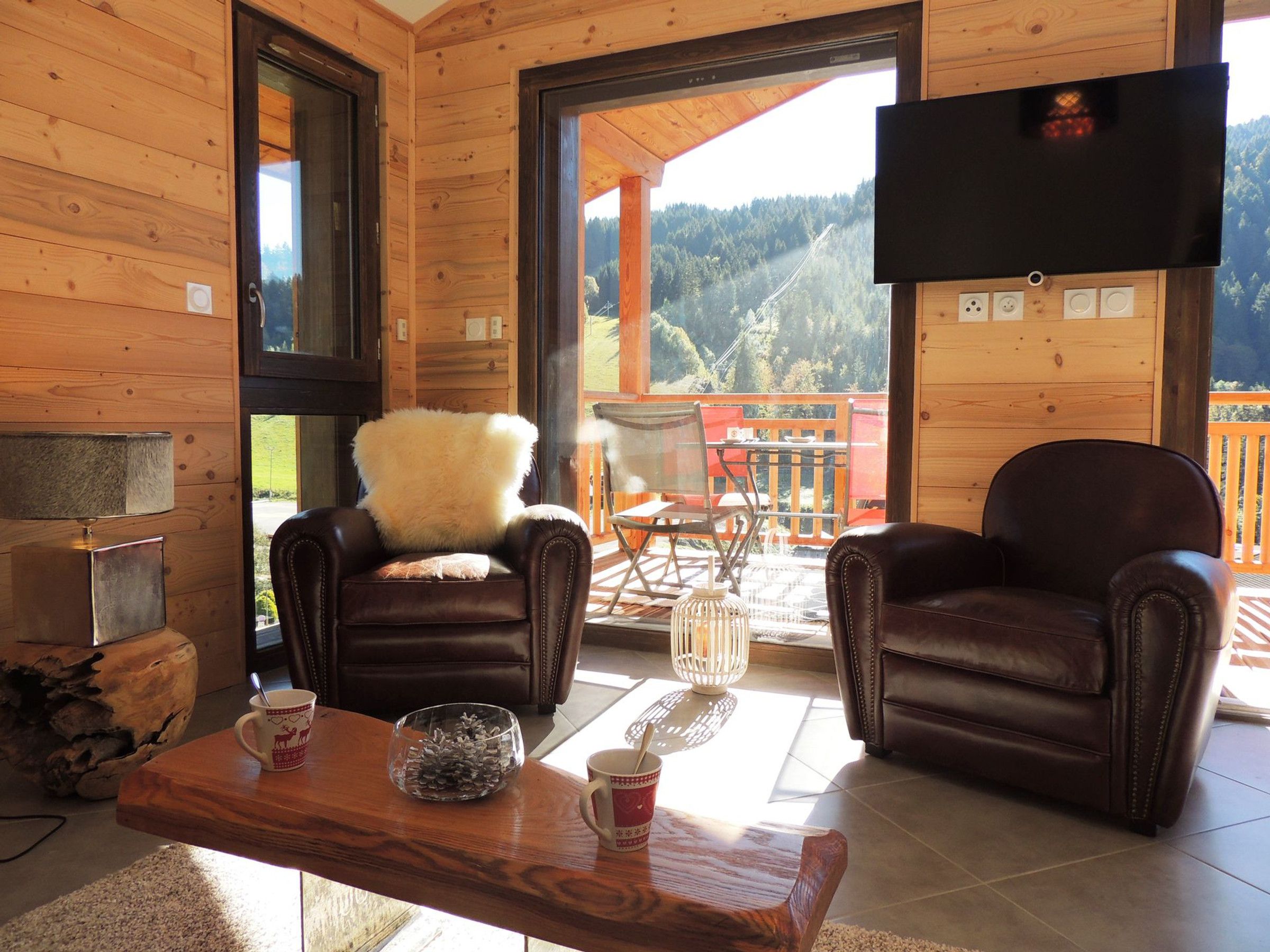Un interior de madera con dos sillones de cuero, una mesa de madera con tazas y un bol de vidrio, y un televisor montado en la pared.