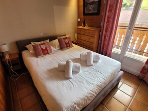 Uma cama bem arrumada com toalhas, um penteadeira de madeira, uma mesa de cabeceira e uma janela com cortinas.
