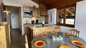 Un interior de madera con una mesa de comedor preparada para cuatro, una zona de cocina con microondas y vistas por una ventana.