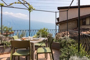 A terrace with a table set for dining, overlooking a scenic view of a lake and mountains.