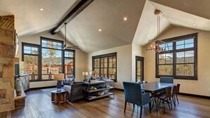 A spacious living room with a large wooden dining table, comfortable seating, and large windows offering views of the outdoors. - Stunning Luxury Home with Private Hot Tub! (Breckenridge)