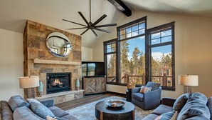 A spacious living room with a stone fireplace, large windows, and a modern ceiling fan. - Stunning Luxury Home with Private Hot Tub! (Breckenridge)