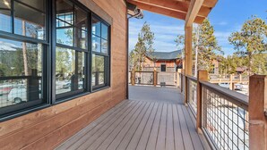 A wooden deck with a railing, large windows, and a view of a building and trees. - Stunning Luxury Home with Private Hot Tub! (Breckenridge)