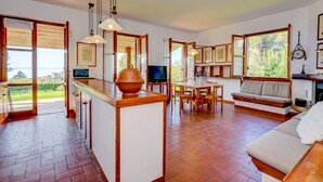A spacious kitchen with a central island, wooden flooring, and a large window offering a view of the outdoors.