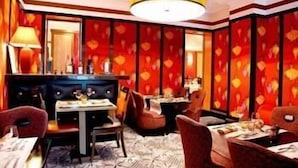 A restaurant with a red patterned wall, a chandelier, and multiple tables with chairs. - Hotel Le Cardinal (Paris)
