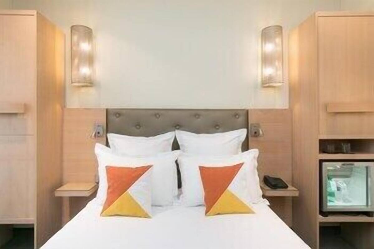 A hotel room with a bed, two bedside tables, a television, and a wardrobe.