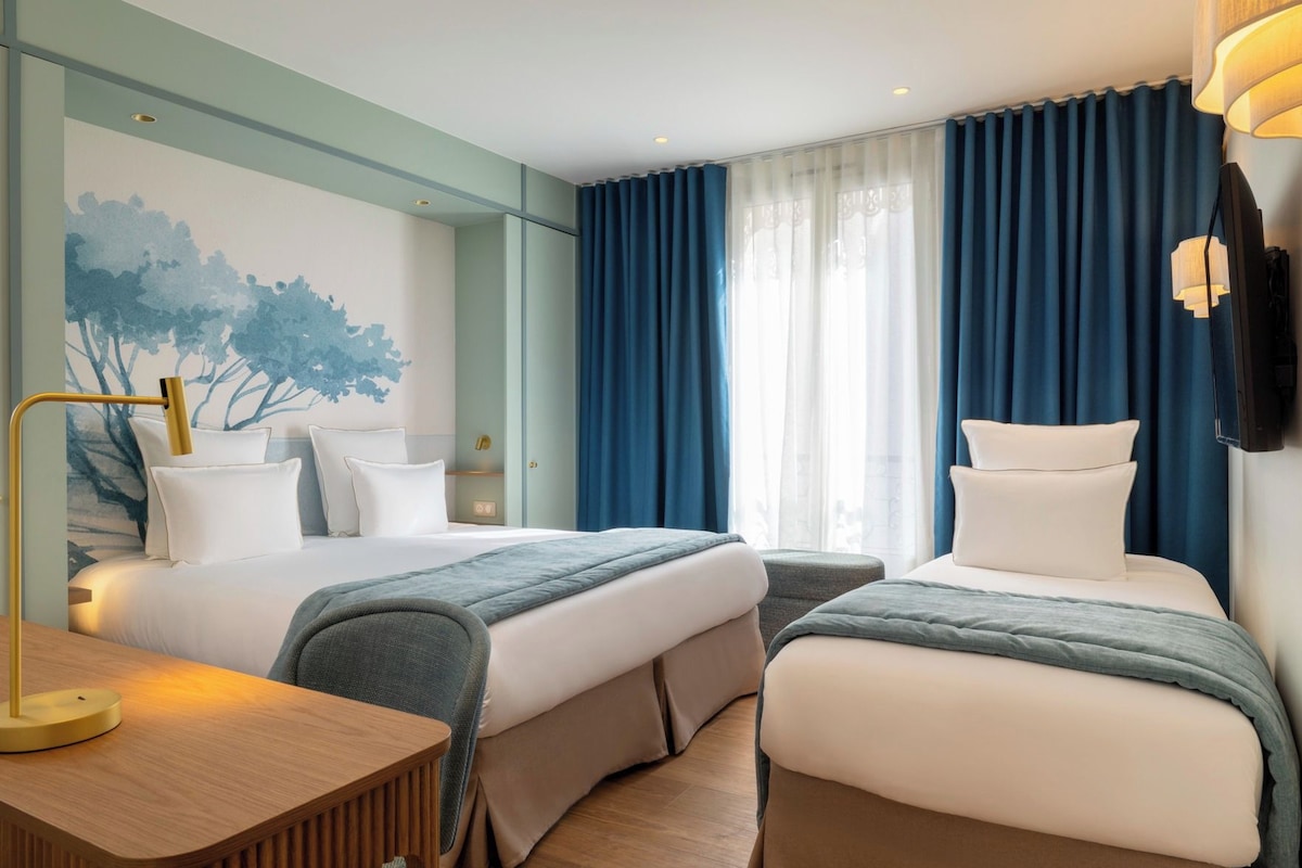 A hotel room with two beds, a desk, a chair, a painting, and a TV.