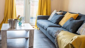 Una sala de estar moderna con un sofá gris, cojines amarillos, una mesa de centro de madera y una maceta de metal sobre la mesa.